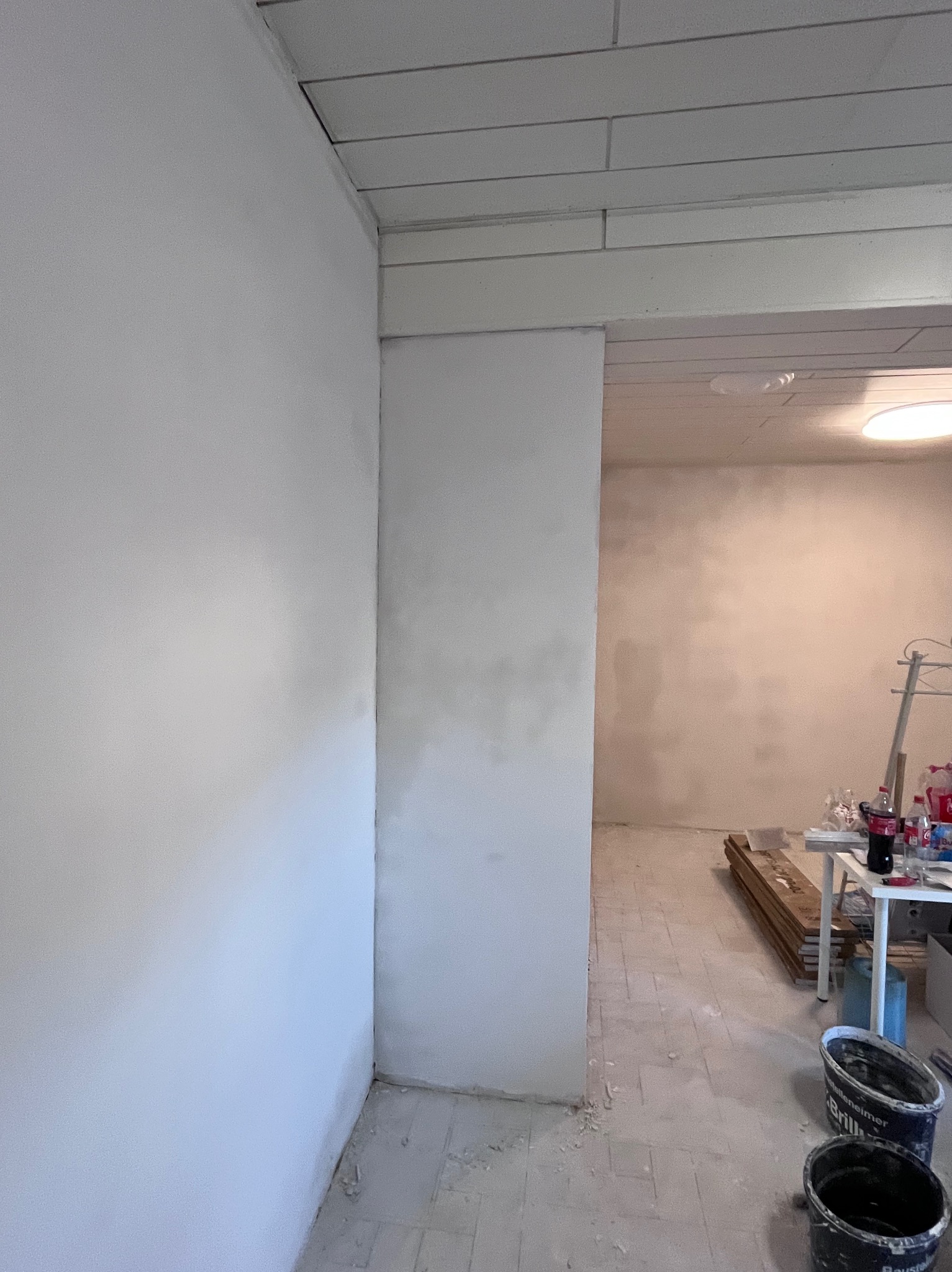 Wnętrze w trakcie prac wykończeniowych, widoczne ściany po nałożeniu gładzi, sufit z drewnianą boazerią, podłoga przygotowana do dalszych prac, dwa wiadra po farbie w dolnym rogu.