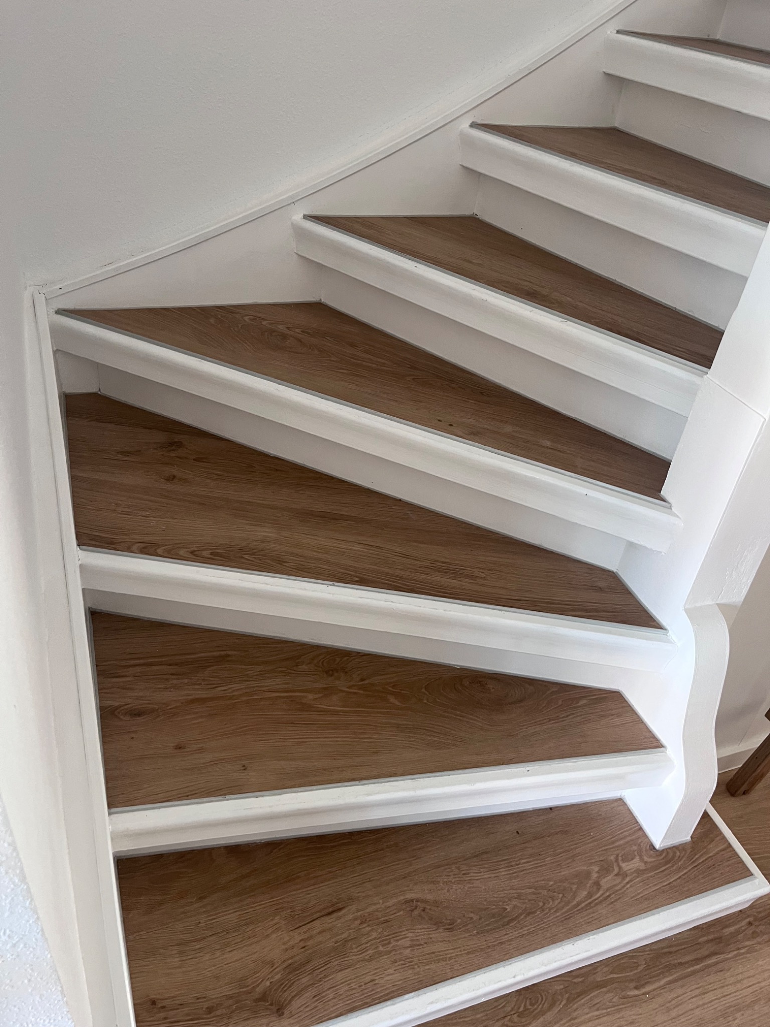 Schody z panelami drewnopodobnymi i białymi listwami wykończeniowymi, widok z dołu, jasne oświetlenie.