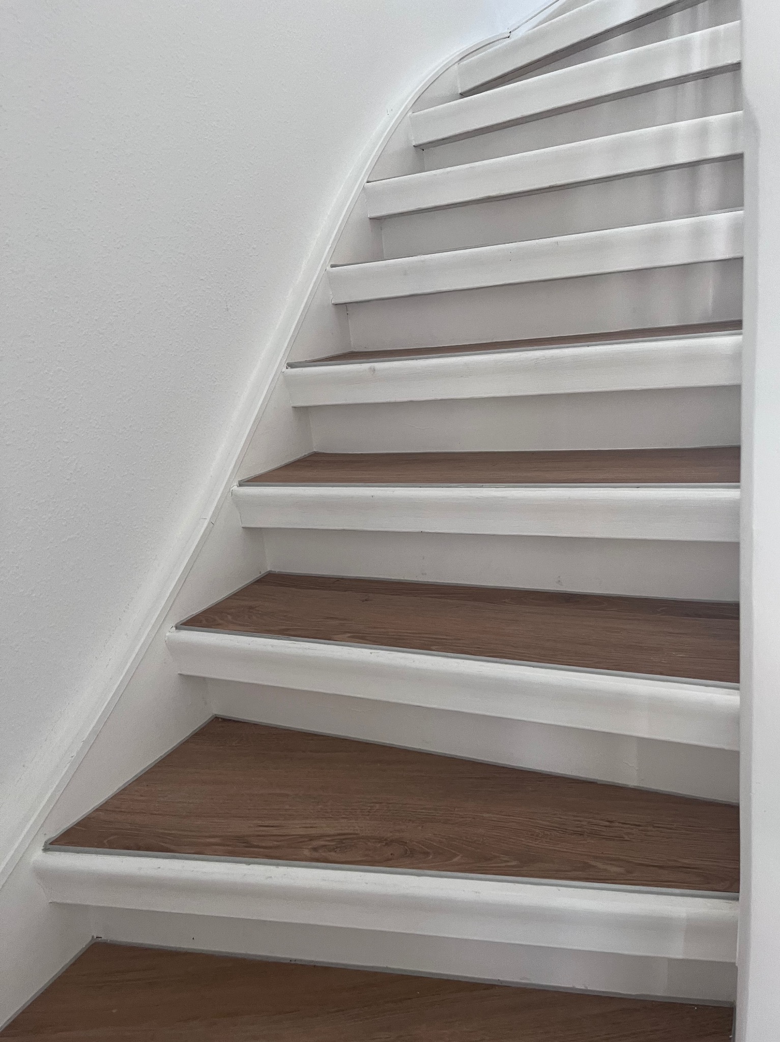 Białe schody z drewnopodobnymi panelami na stopniach, widok z dołu, akcent na detale wykończenia.