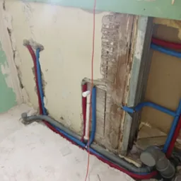 Instalacja wodno-kanalizacyjna w trakcie remontu łazienki: rury w izolacji, surowe ściany, widoczne elementy starej konstrukcji. Etap prac przed wykończeniem.