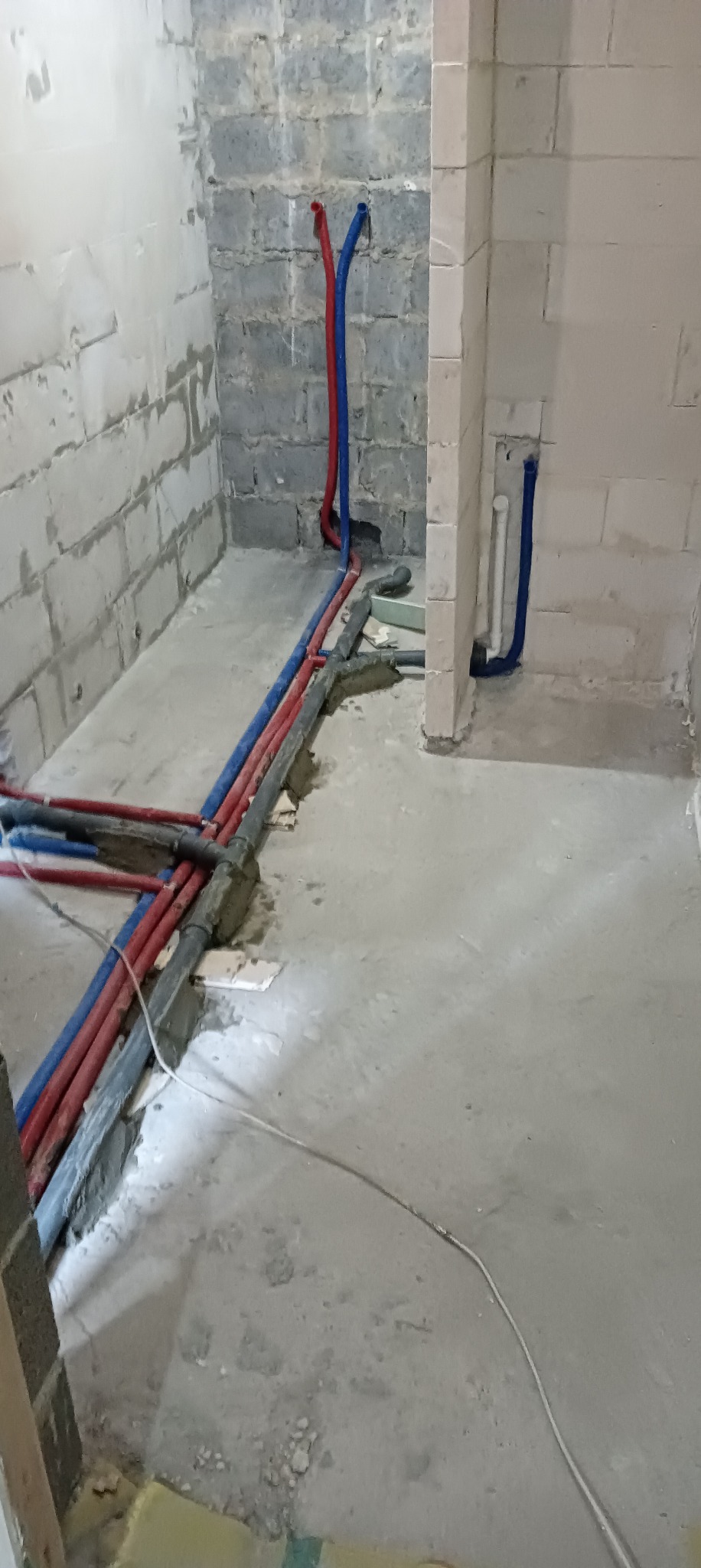 Surowa łazienka w trakcie remontu z widocznymi rurami instalacji wodnej (czerwone i niebieskie) wychodzącymi ze ściany z betonu komórkowego.