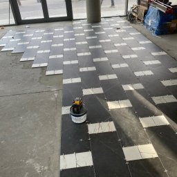 Majsterpro - Układanie płytek podłogowych w szachownicę, z użyciem krzyżyków dystansowych i poziomicy laserowej, na surowym podłożu w jasnym wnętrzu.