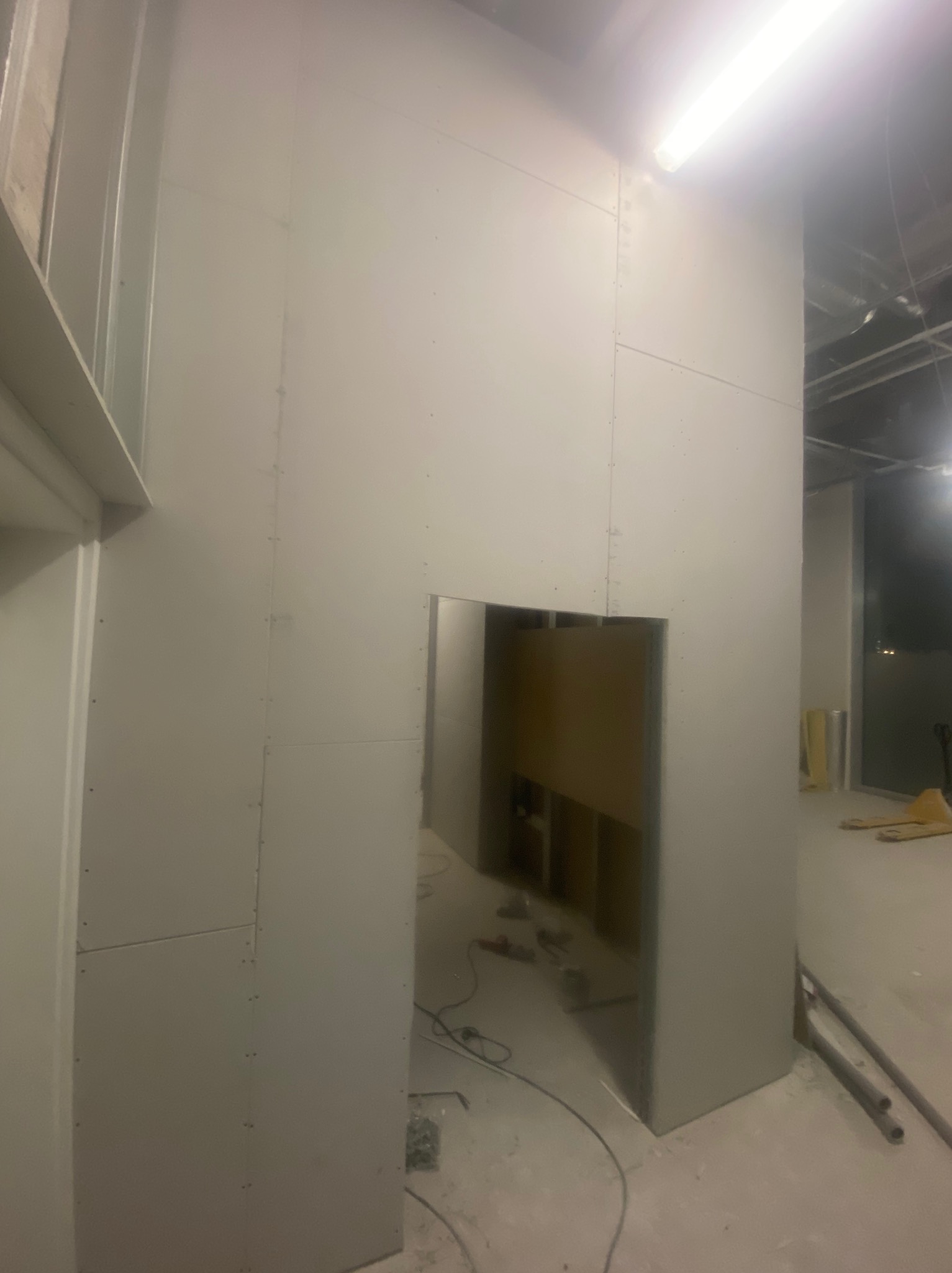 Wnętrze w trakcie prac: ściany z płyt kartonowo-gipsowych, widoczne łączenia i otwór drzwiowy. Przewody na podłodze sugerują dalsze prace instalacyjne.