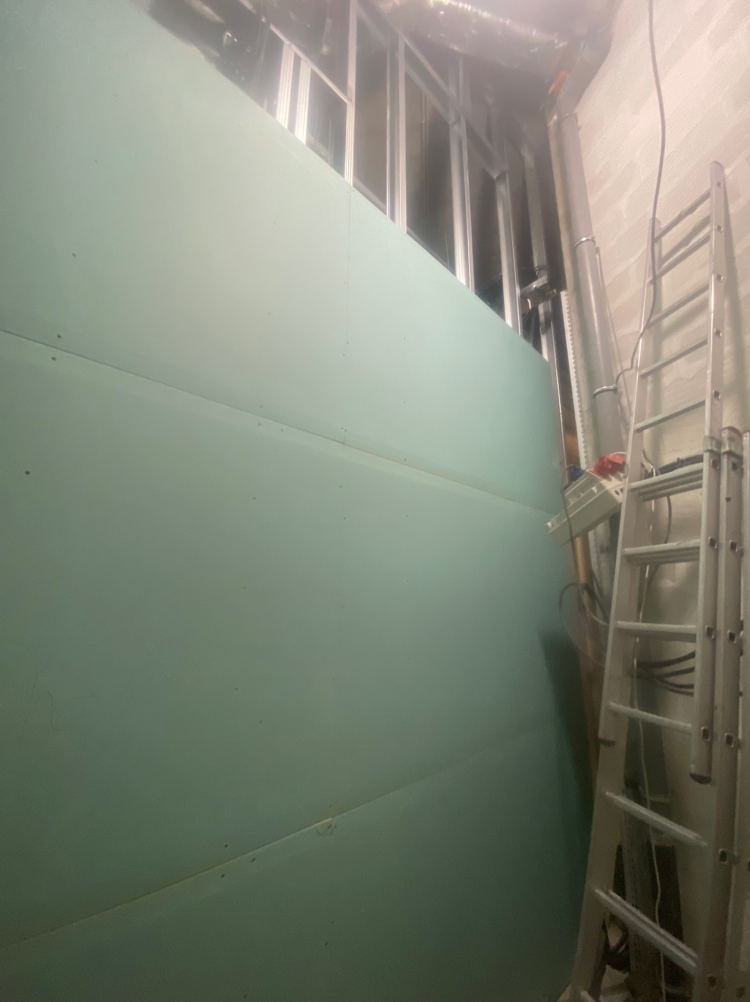 Montaż płyty karton-gips na metalowym stelażu, widoczna drabina i instalacje. Etap prac wykończeniowych w pomieszczeniu.