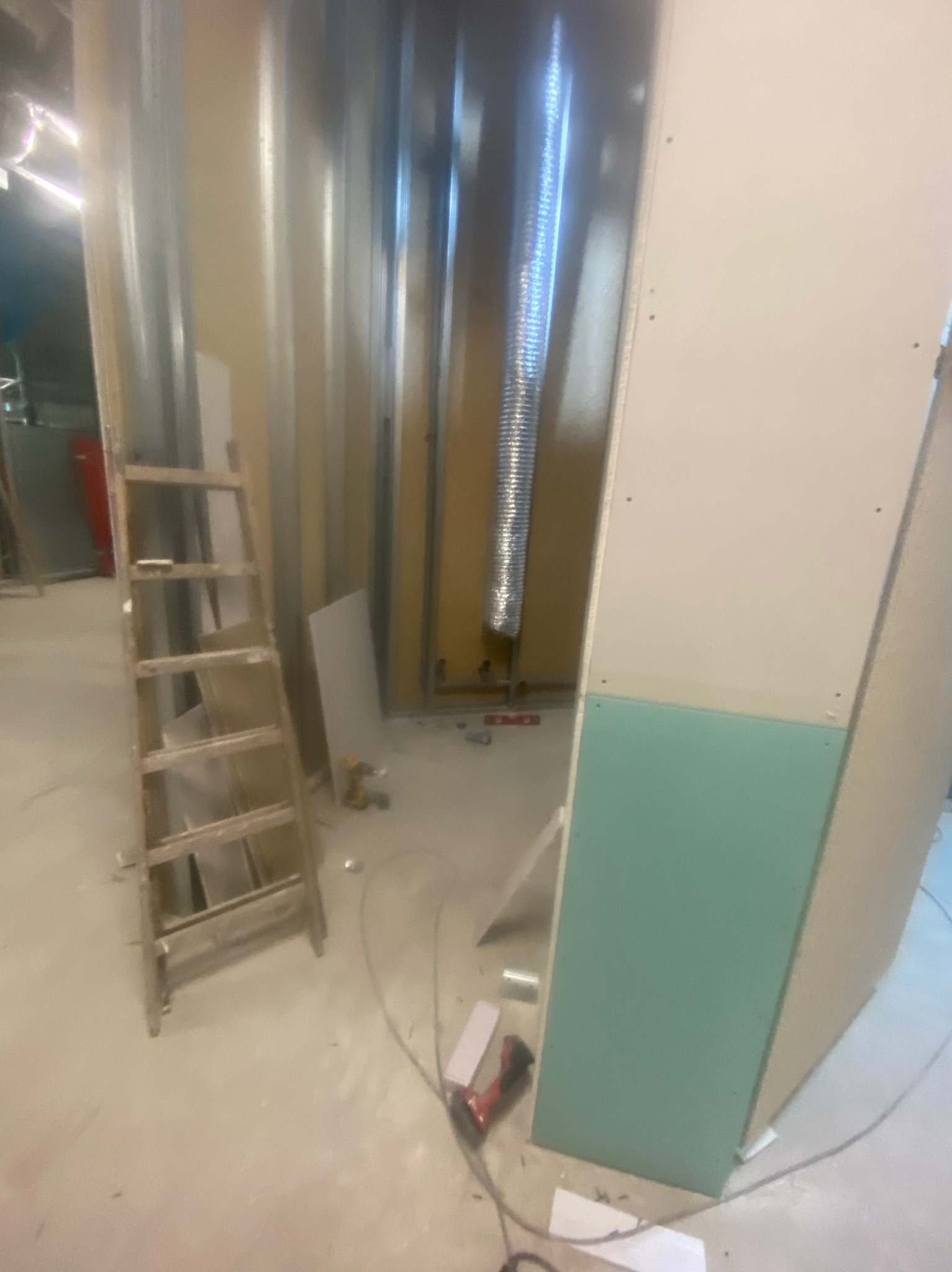 Montaż płyt gipsowych w surowym wnętrzu z widoczną instalacją wentylacyjną i drewnianą drabiną. Etap prac wykończeniowych.