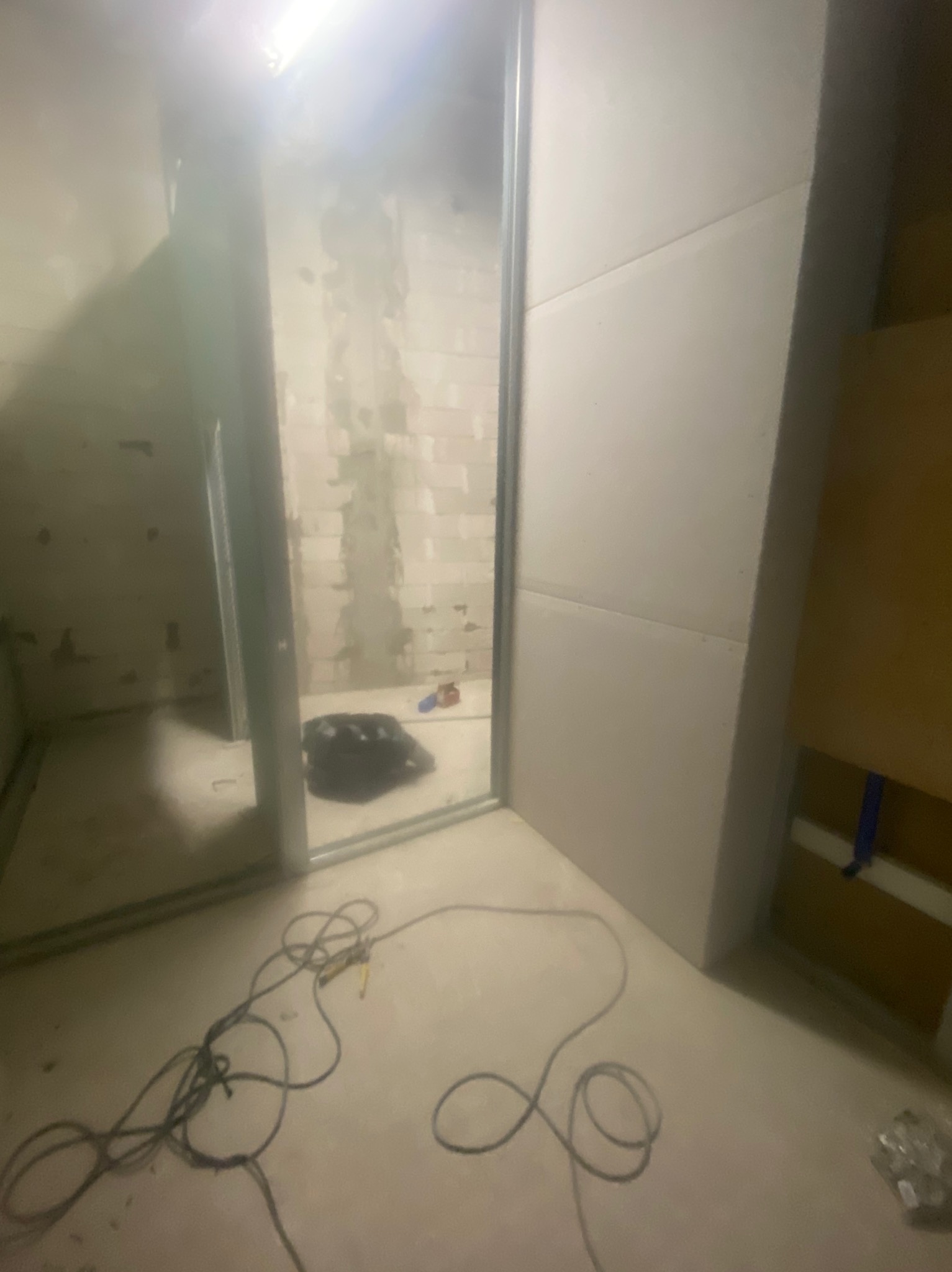 Wnętrze w trakcie prac wykończeniowych: widoczne płyty gipsowo-kartonowe na ścianach, metalowe profile i przewody na podłodze. Częściowo wykończone ściany w tle.