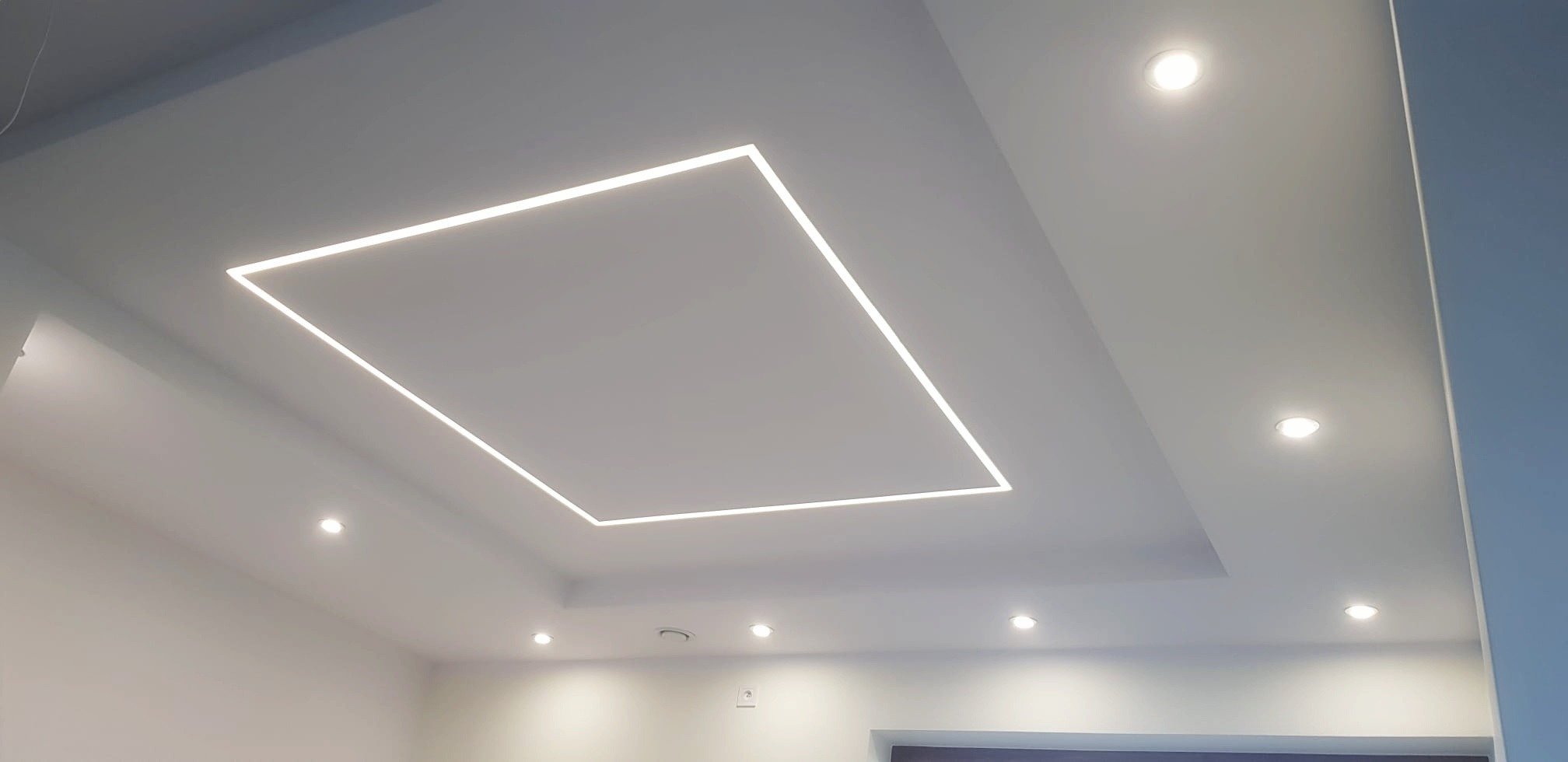 Nowoczesny sufit podwieszany z oświetleniem LED w kształcie kwadratu i punktowymi lampami halogenowymi, białe ściany.