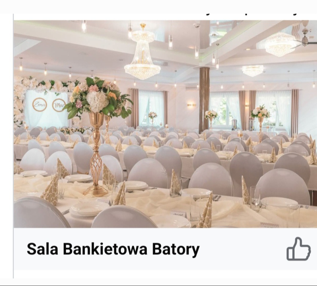 Elegancka sala bankietowa z białymi krzesłami, stołami nakrytymi kremowymi obrusami i kwiatowymi dekoracjami. Kryształowe żyrandole oświetlają przestrzeń.