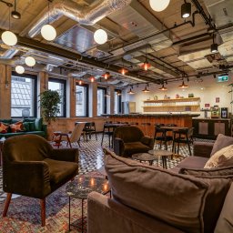 WORKSPACE-SERVICE - Przestronne wnętrze biurowe z sofami, fotelami i barem, oświetlone kulistymi lampami, z widocznymi elementami instalacji na suficie.