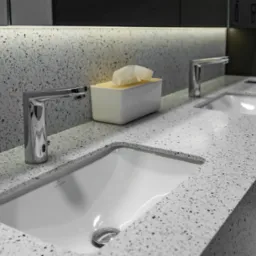 Biała umywalka Villeroy & Boch wkomponowana w blat z szarego lastryko, chromowana bateria, dozownik na chusteczki higieniczne w tle, oświetlenie LED pod szafką.