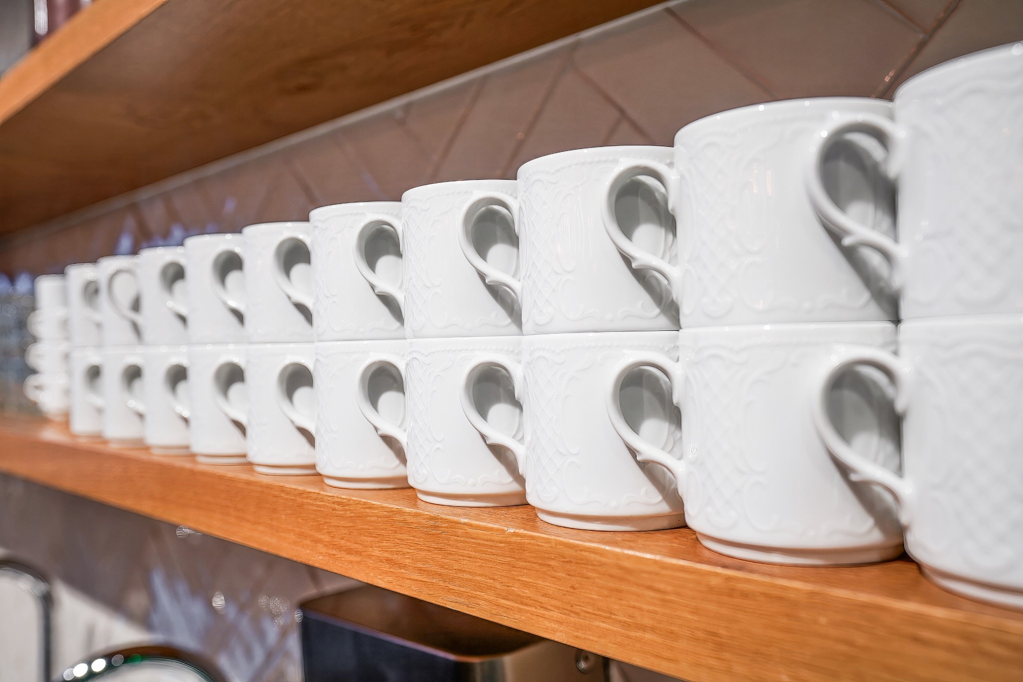 Rząd ułożonych w stosy białych filiżanek z wytłaczanym wzorem na drewnianej półce w biurze.