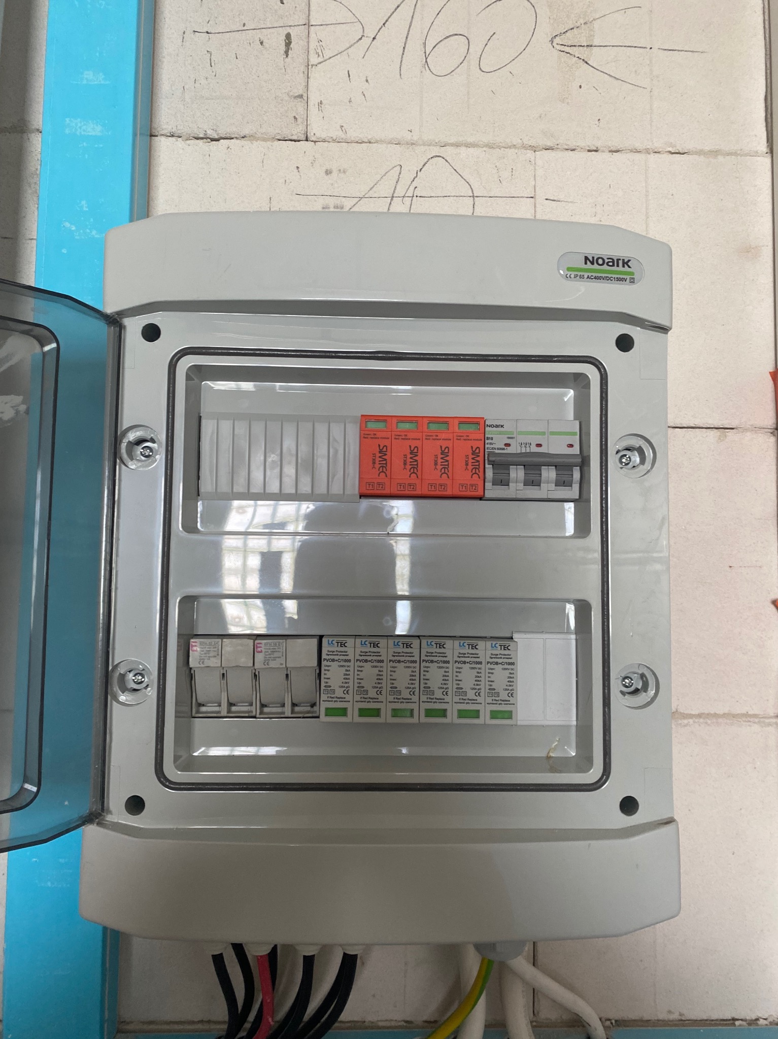 Otwarta skrzynka elektryczna Noark z zabezpieczeniami SIMTEC i LCTEC, widoczne przewody. Montaż w surowym wnętrzu.