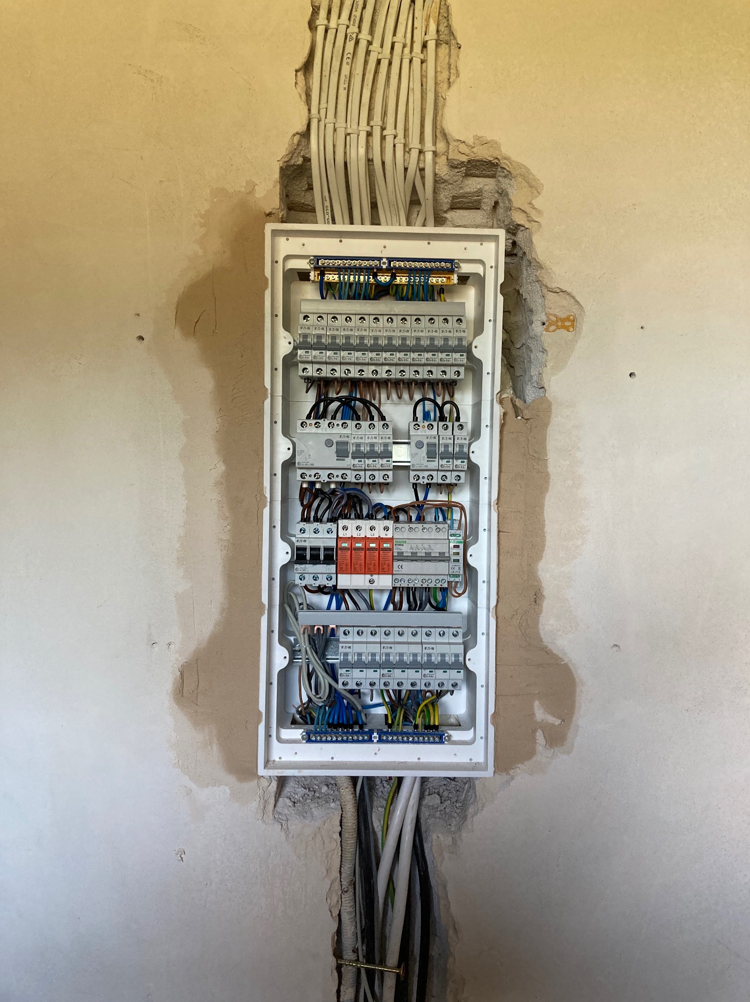 Otwarta skrzynka z bezpiecznikami i przewodami w surowej ścianie. Widoczne kable wchodzące od góry i dołu, oraz elementy instalacji wewnątrz skrzynki.