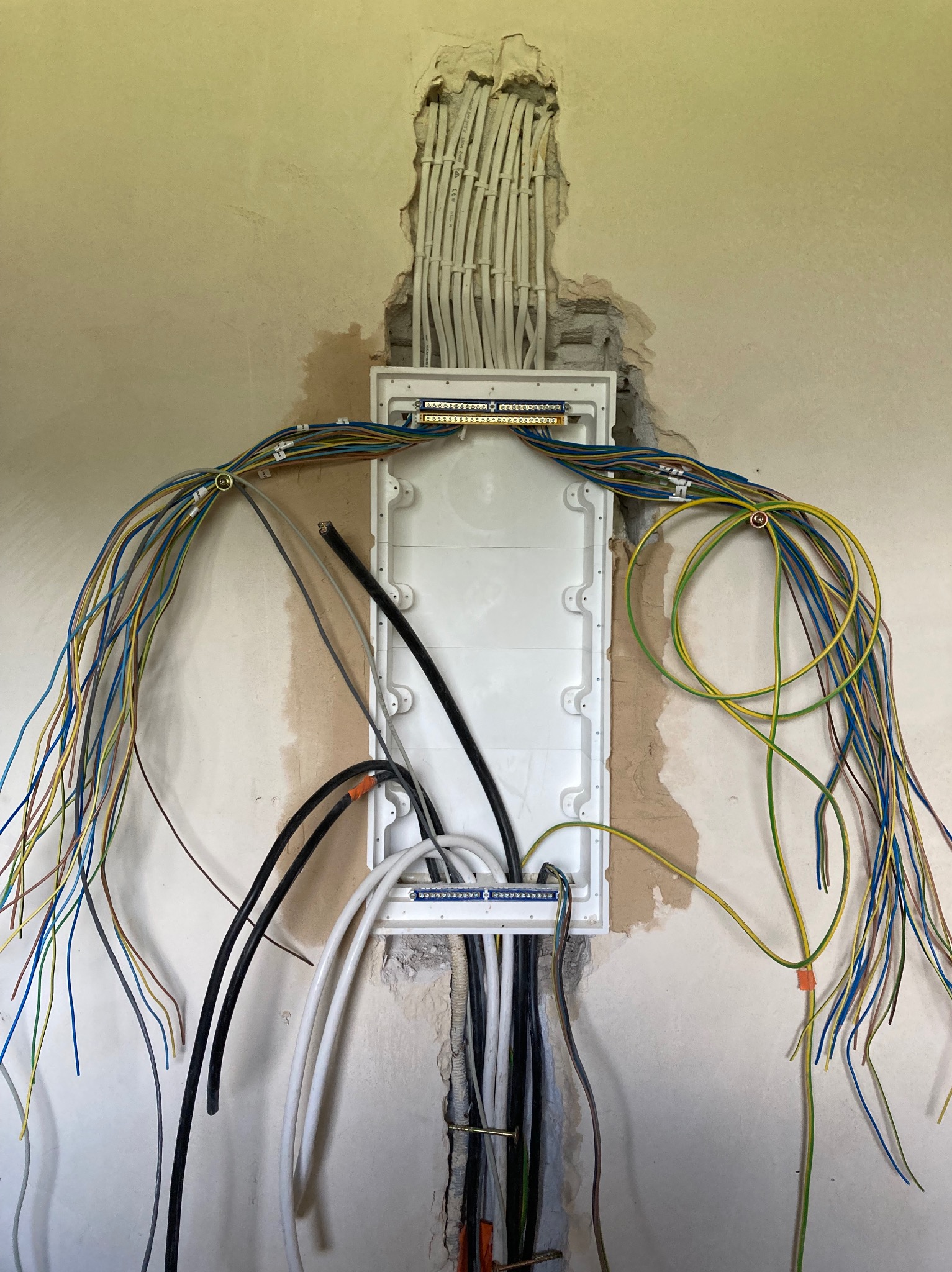 Rozdzielnica elektryczna w trakcie montażu w ścianie, widoczne kable w różnych kolorach i przekrojach, ściana z widocznymi śladami po kuciu.