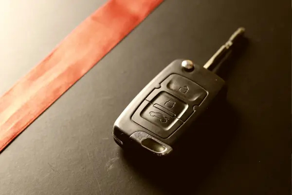 Kluczyk samochodowy z pilotem leżący na czarnym tle z czerwoną wstążką, sugerujący prezent lub wygraną.