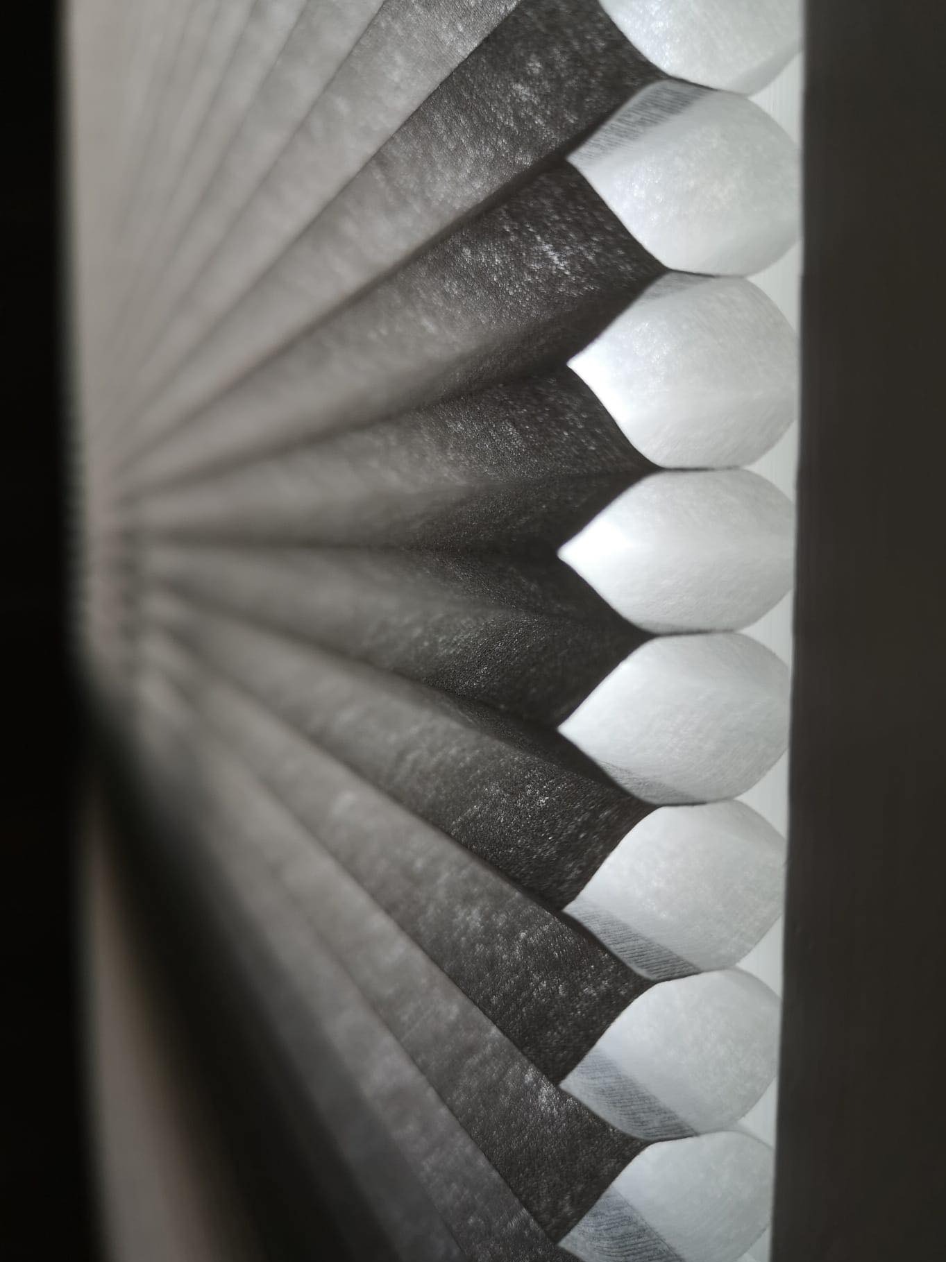 Detaliczny widok z bliska na szare plisowane rolety w strukturze plastra miodu, ukazujący ich izolacyjne właściwości oraz nowoczesny design.