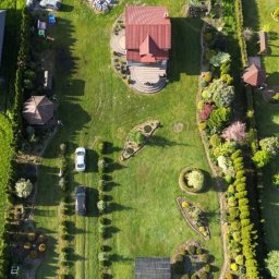 Mariusz Oraczewski - Zdjęcie z drona przedstawiające zadbany ogród z domem, dwoma samochodami, panelami słonecznymi i altaną, otoczony żywopłotem.