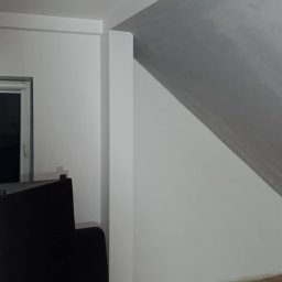 adamczakrenovaties - Pokój na poddaszu po remoncie: świeżo pomalowane ściany w odcieniach bieli i szarości, drewniana podłoga, czarna sofa i nowoczesna lampa sufitowa.