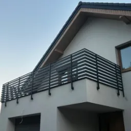 Nowoczesna, pozioma, czarna balustrada balkonowa z metalowych profili na tle białej elewacji domu jednorodzinnego w słoneczny dzień. Minimalistyczny design.