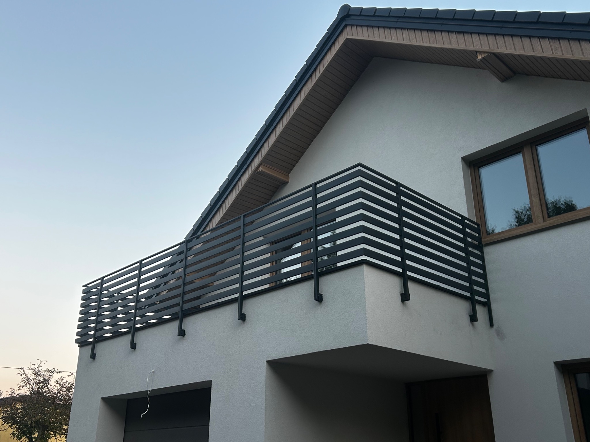 Nowoczesna, pozioma, czarna balustrada balkonowa z metalowych profili na tle białej elewacji domu jednorodzinnego w słoneczny dzień. Minimalistyczny design.