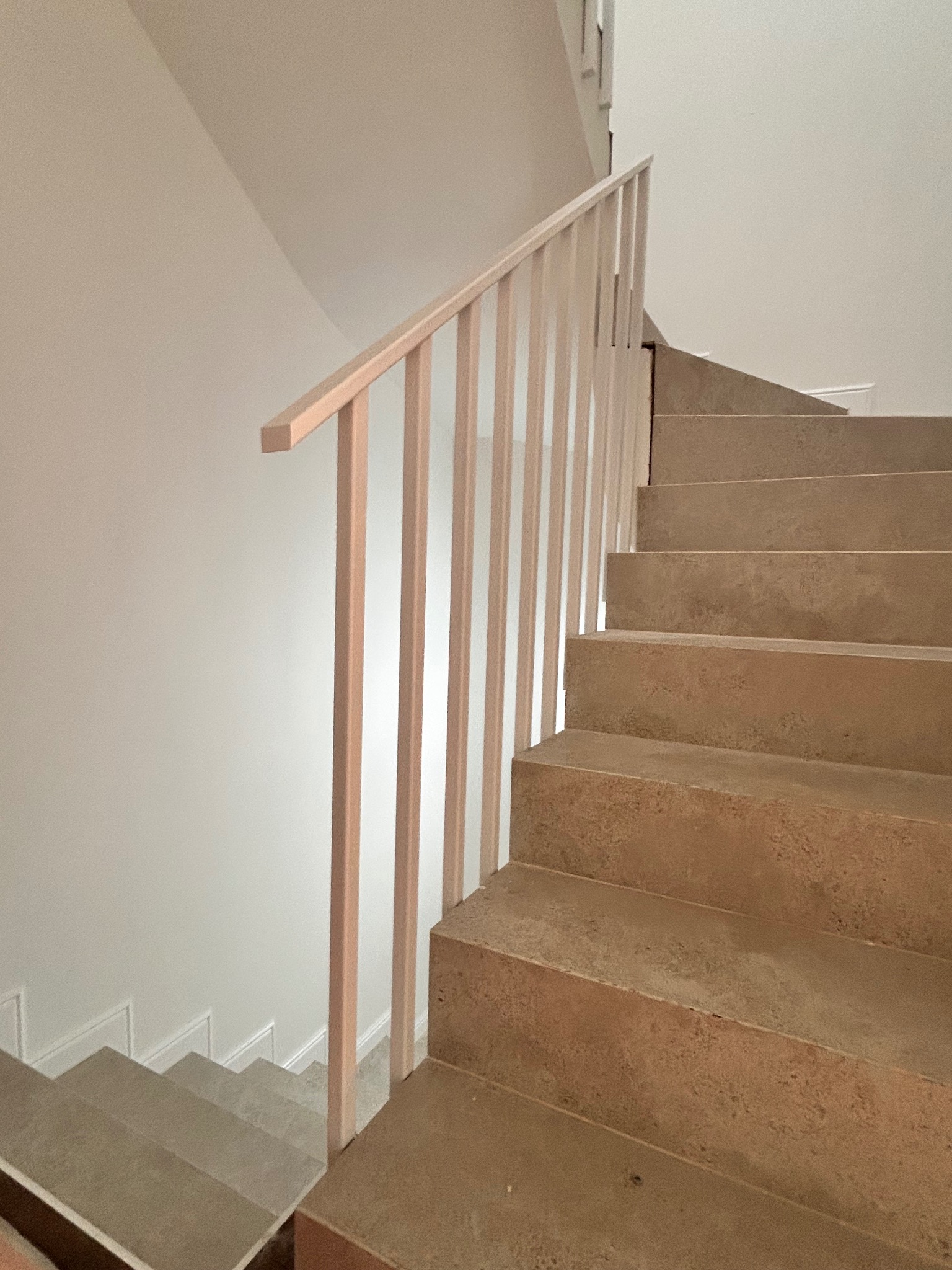 Betonowe schody z jasną, minimalistyczną balustradą z pionowych słupków. Ujęcie z dołu, podkreślające surowy charakter materiałów i prostotę formy.