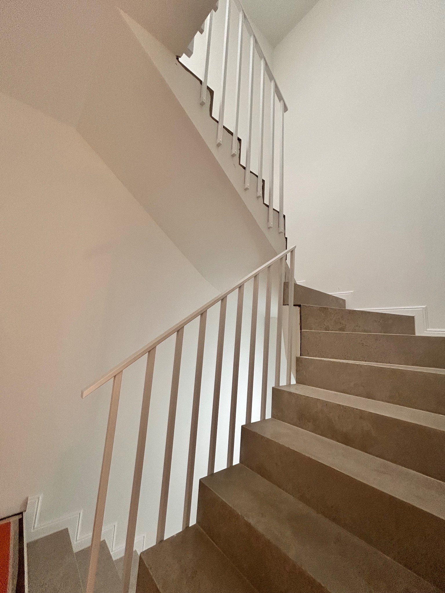 Minimalistyczne schody betonowe z jasną balustradą, widok z dołu, podkreślający surowy charakter wnętrza i geometryczny układ stopni.