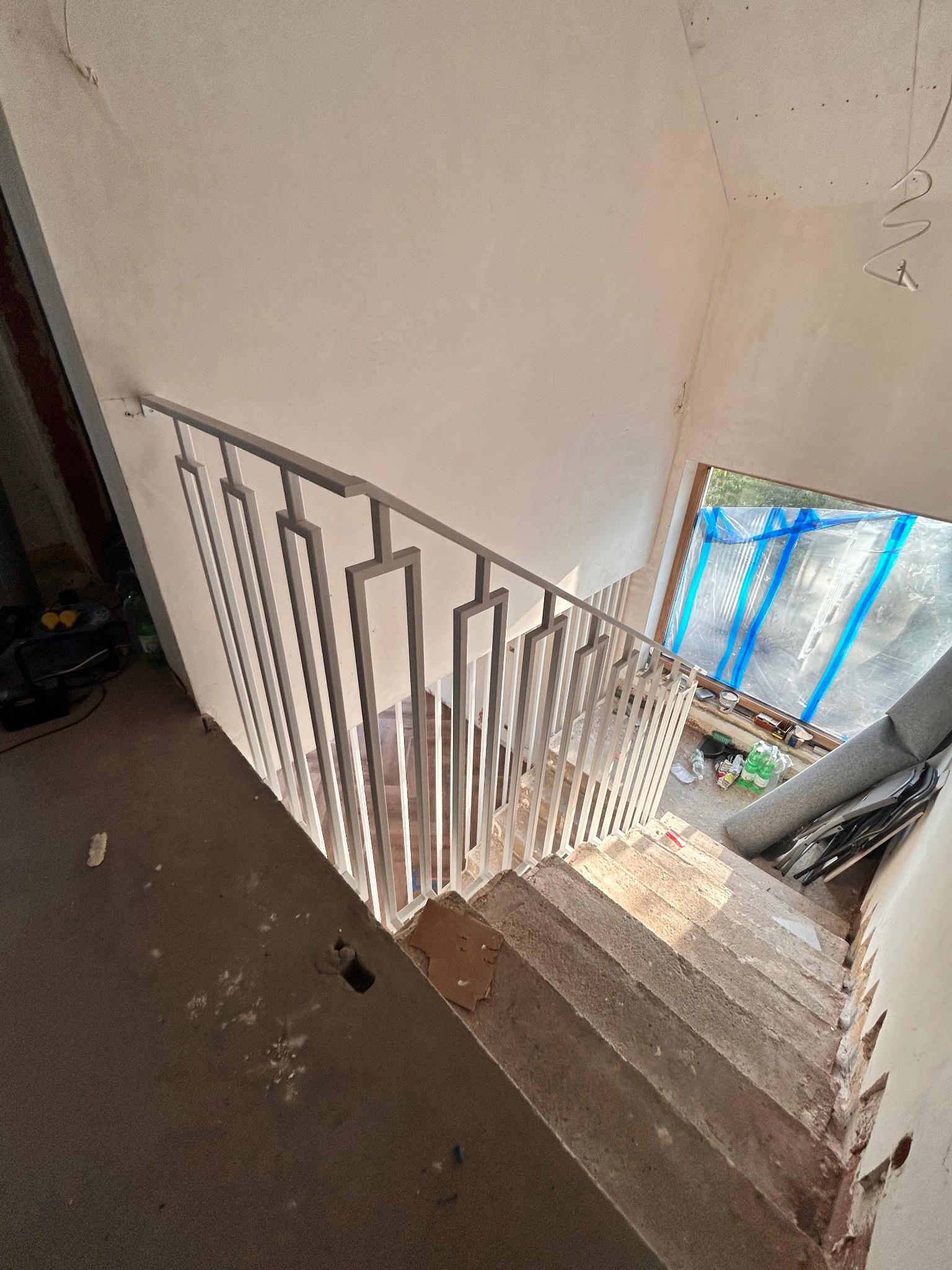 Nowoczesna, metalowa balustrada schodowa z geometrycznym wzorem, zamontowana na surowych, betonowych schodach w trakcie remontu. Widok z góry.