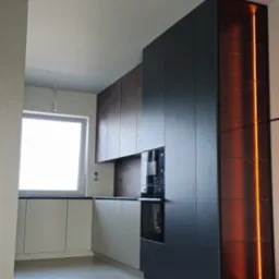 Nowoczesna kuchnia z szarymi i brązowymi szafkami, wbudowanym piekarnikiem i oświetloną pionową witryną, na podłodze widoczne materiały zabezpieczające podczas montażu.