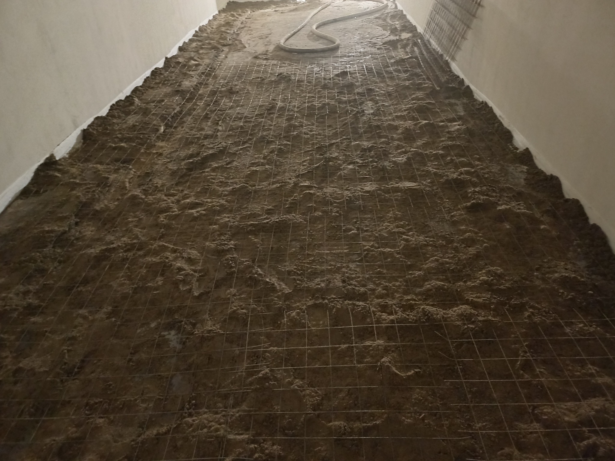 Przygotowanie podłoża pod wylewkę z siatką zbrojeniową i wężem do rozprowadzania masy w pomieszczeniu.