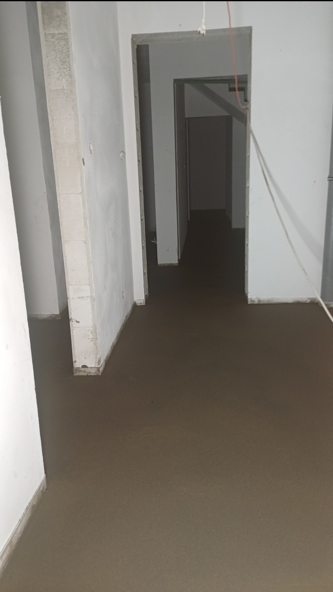 Świeżo wylana, brązowa posadzka w korytarzu z widocznymi otworami drzwiowymi w Pokrzywnicy, w trakcie prac wykończeniowych.