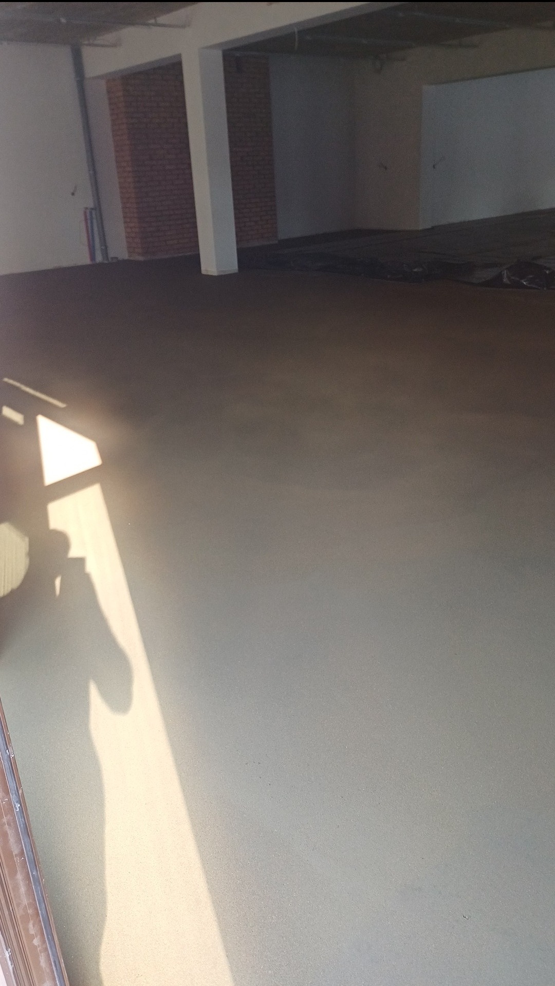 Świeżo wylana, gładka posadzka jastrychowa w surowym wnętrzu z widocznym cieniem osoby robiącej zdjęcie wpadającym przez okno.