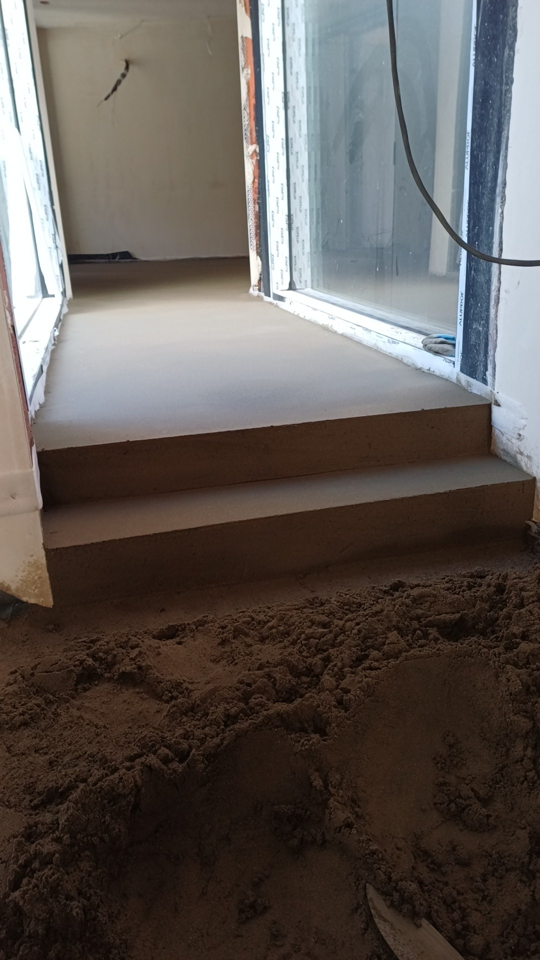 Wylewka betonowa schodów wewnętrznych w trakcie realizacji, widoczne okna i przygotowany materiał.