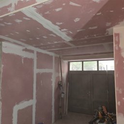 Kmk team sp zoo - Ściana i sufit z płyt gipsowo-kartonowych w trakcie szpachlowania; widoczne narzędzia i materiały budowlane, surowe wykończenie wnętrza przed malowaniem.