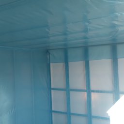 Kmk team sp zoo - Pokój zabezpieczony folią i taśmą malarską przed remontem, widoczne ramy okienne i podłoga. Przygotowanie pomieszczenia do prac wykończeniowych, ochrona przed zabrudzeniami.