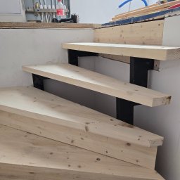 Kmk team sp zoo - Wnętrze w trakcie remontu: drewniane schody z czarnymi wspornikami, instalacja hydrauliczna na ścianie. Widoczne narzędzia i materiały budowlane.