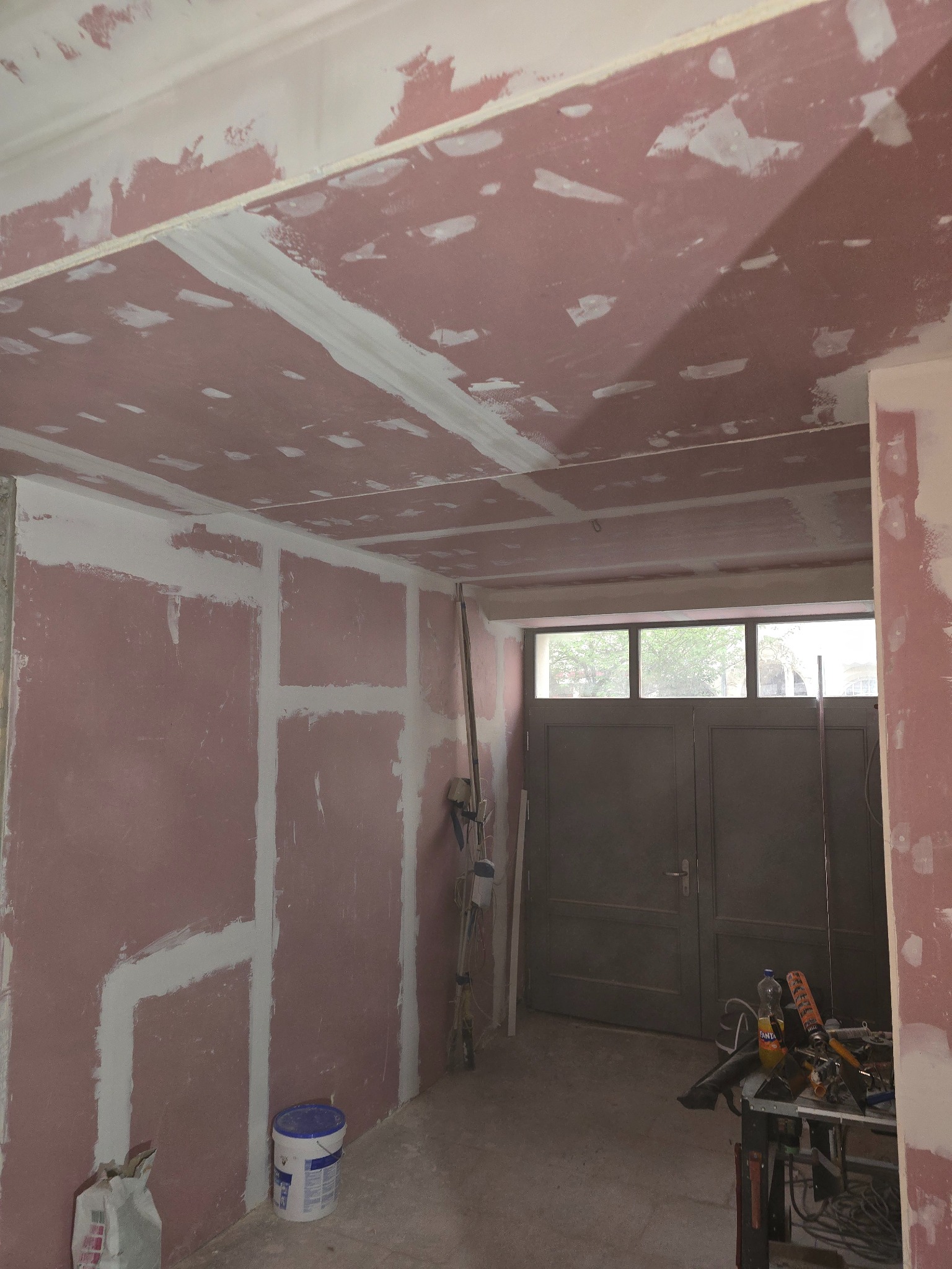 Ściana i sufit z płyt gipsowo-kartonowych w trakcie szpachlowania; widoczne narzędzia i materiały budowlane, surowe wykończenie wnętrza przed malowaniem.