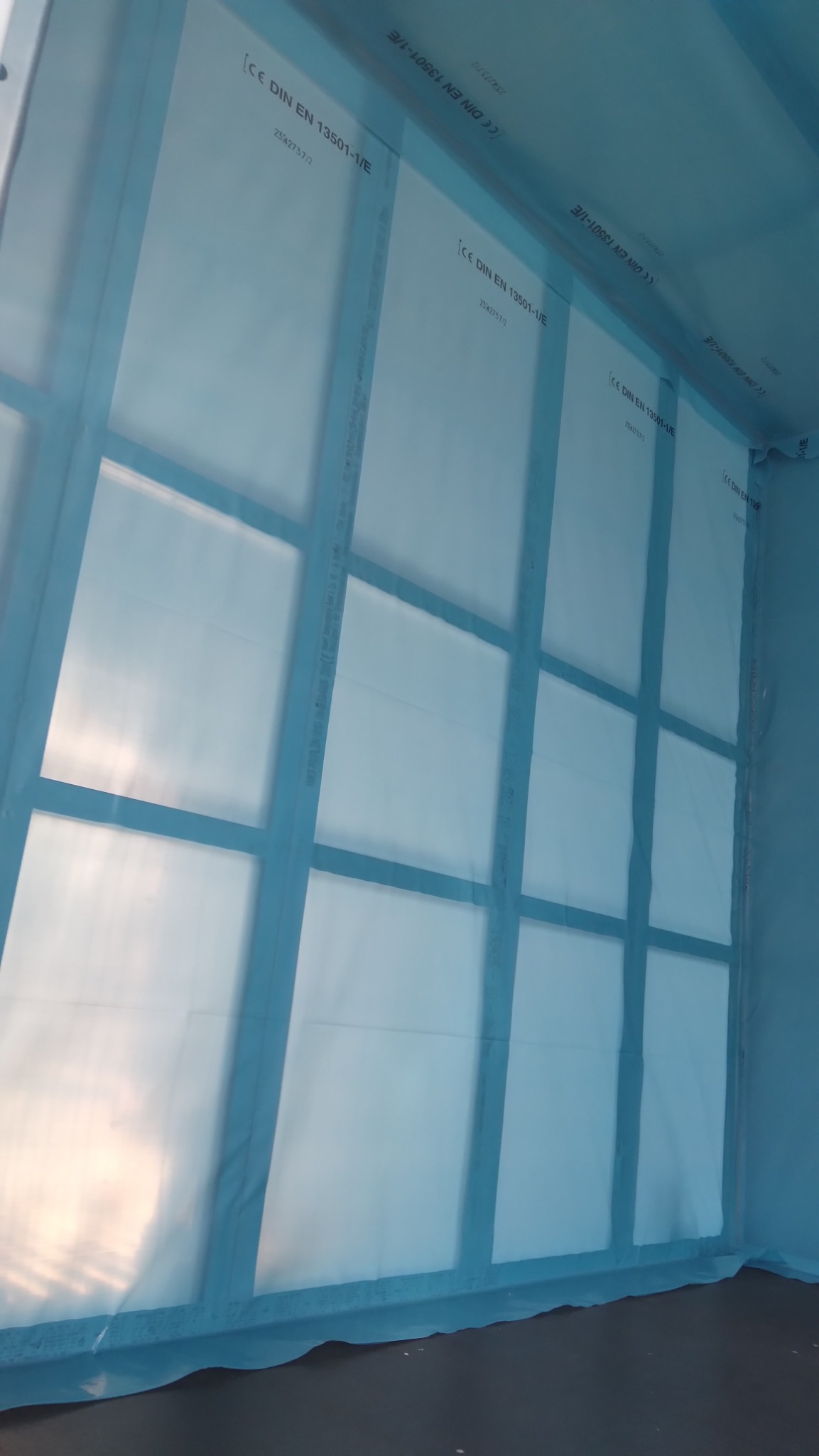Wnętrze osłonięte folią z oznaczeniami CE DIN EN 13501-1/E, widoczne ramy konstrukcji. Ochrona podczas prac remontowych lub budowlanych.