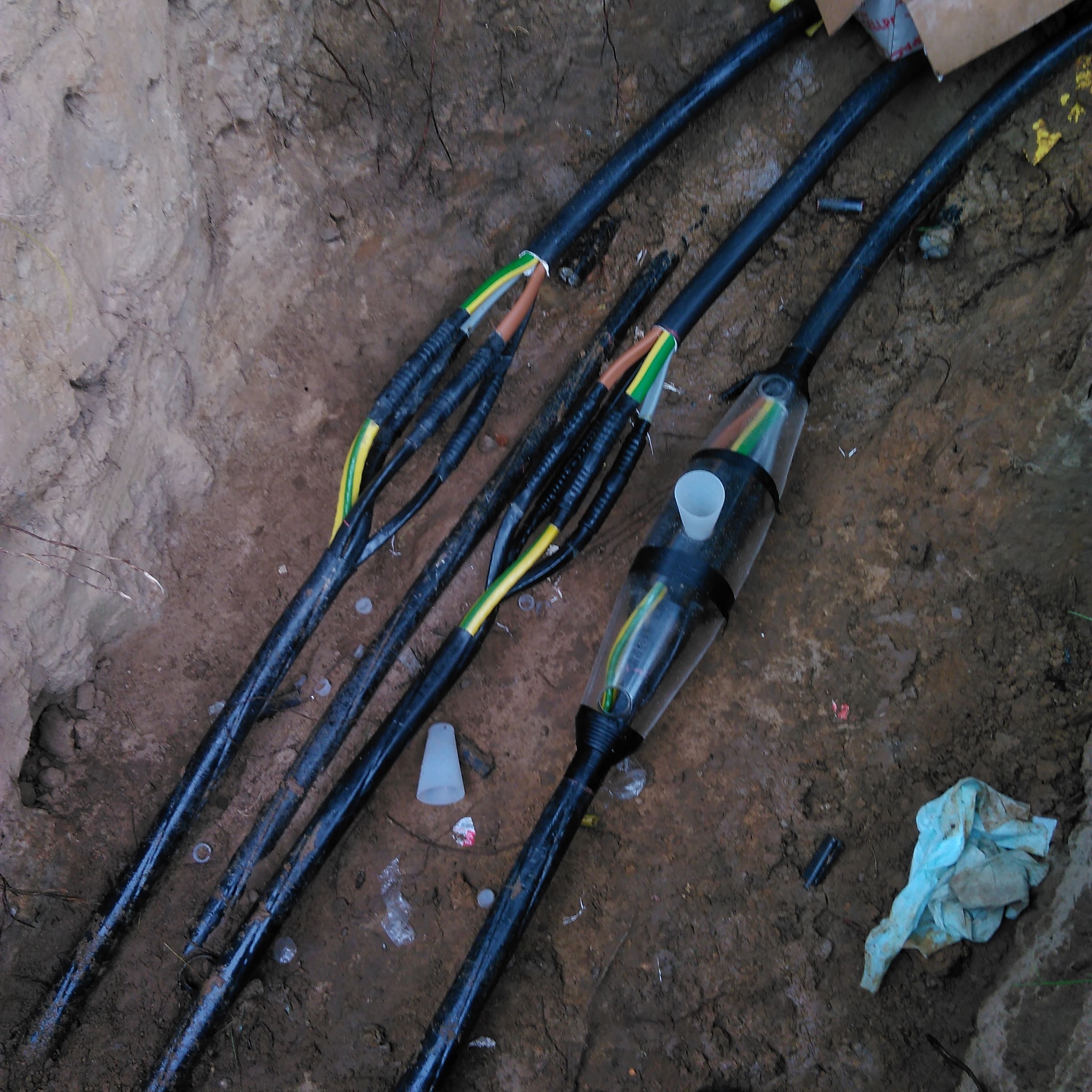 Podziemne kable energetyczne w wykopie, widoczne złącza kablowe z elementami izolacji termokurczliwej i zakończeniami przewodów w kolorach żółto-zielonym, brązowym i szarym.