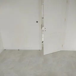 Jasne, marmurowe płytki podłogowe w nowym pomieszczeniu z białymi ścianami i otwartymi, białymi drzwiami. Widoczne listwy przypodłogowe i instalacja elektryczna.