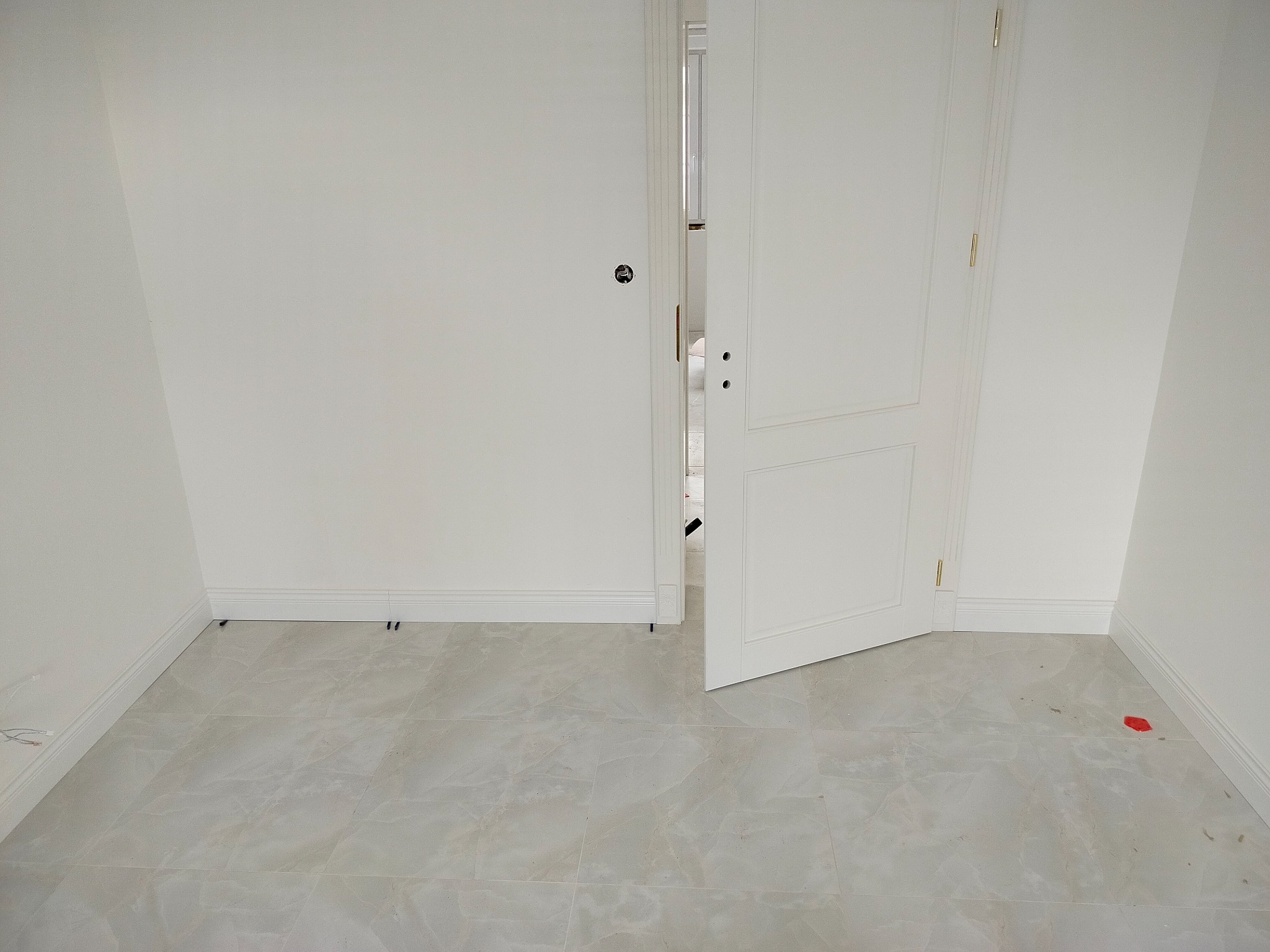 Jasne, marmurowe płytki podłogowe w nowym pomieszczeniu z białymi ścianami i otwartymi, białymi drzwiami. Widoczne listwy przypodłogowe i instalacja elektryczna.