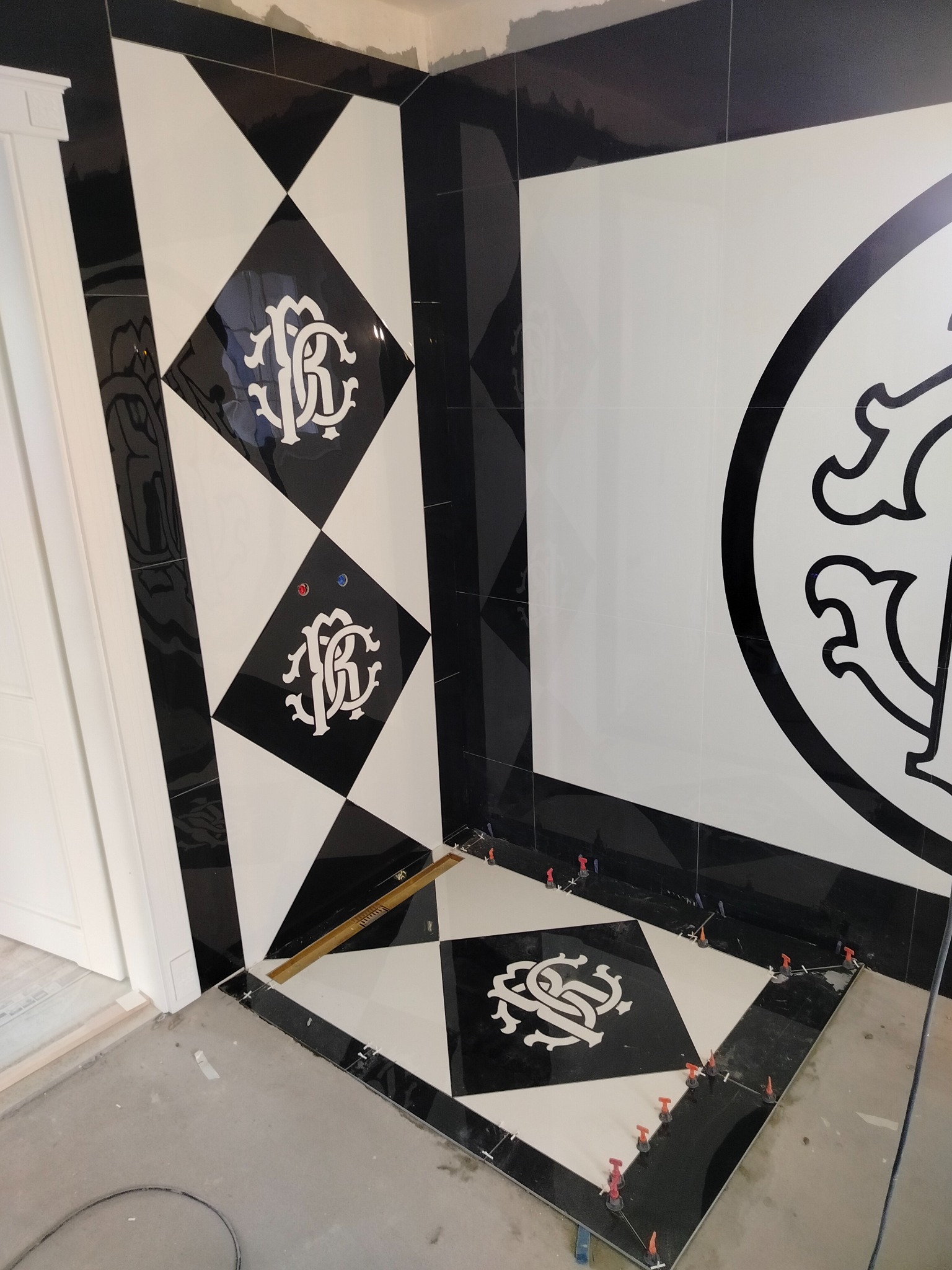 Czarno-białe płytki z wzorem ułożone na ścianie i podłodze w rogu łazienki, z widocznymi elementami poziomowania płytek. Nietypowy wzór.