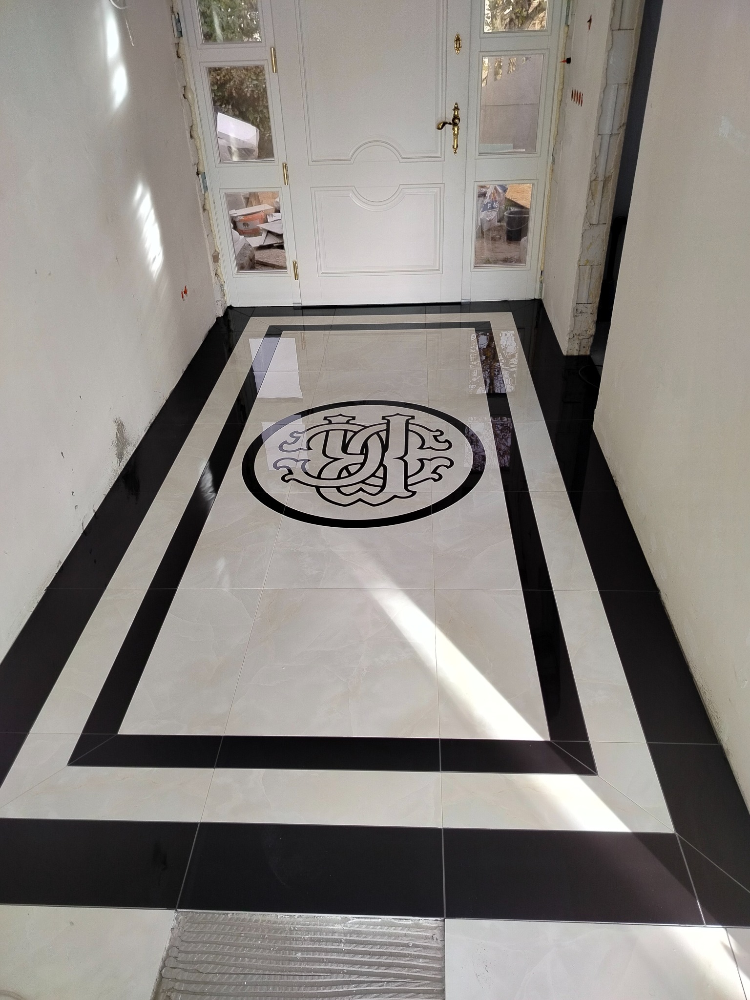 Elegancka posadzka z jasnych i czarnych płytek, z dekoracyjnym motywem pośrodku, ułożona w korytarzu przy wejściu do domu, widok z góry.