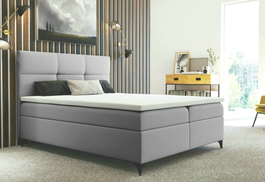 Szare łóżko kontynentalne z pikowanym zagłówkiem i białym materacem nawierzchniowym w nowoczesnej sypialni z drewnianymi panelami ściennymi i minimalistycznym stolikiem nocnym.