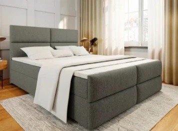 Szare łóżko kontynentalne z tapicerowanym wezgłowiem i materacem nawierzchniowym w Zduńskiej Woli, ustawione na dywanie w geometryczne wzory.