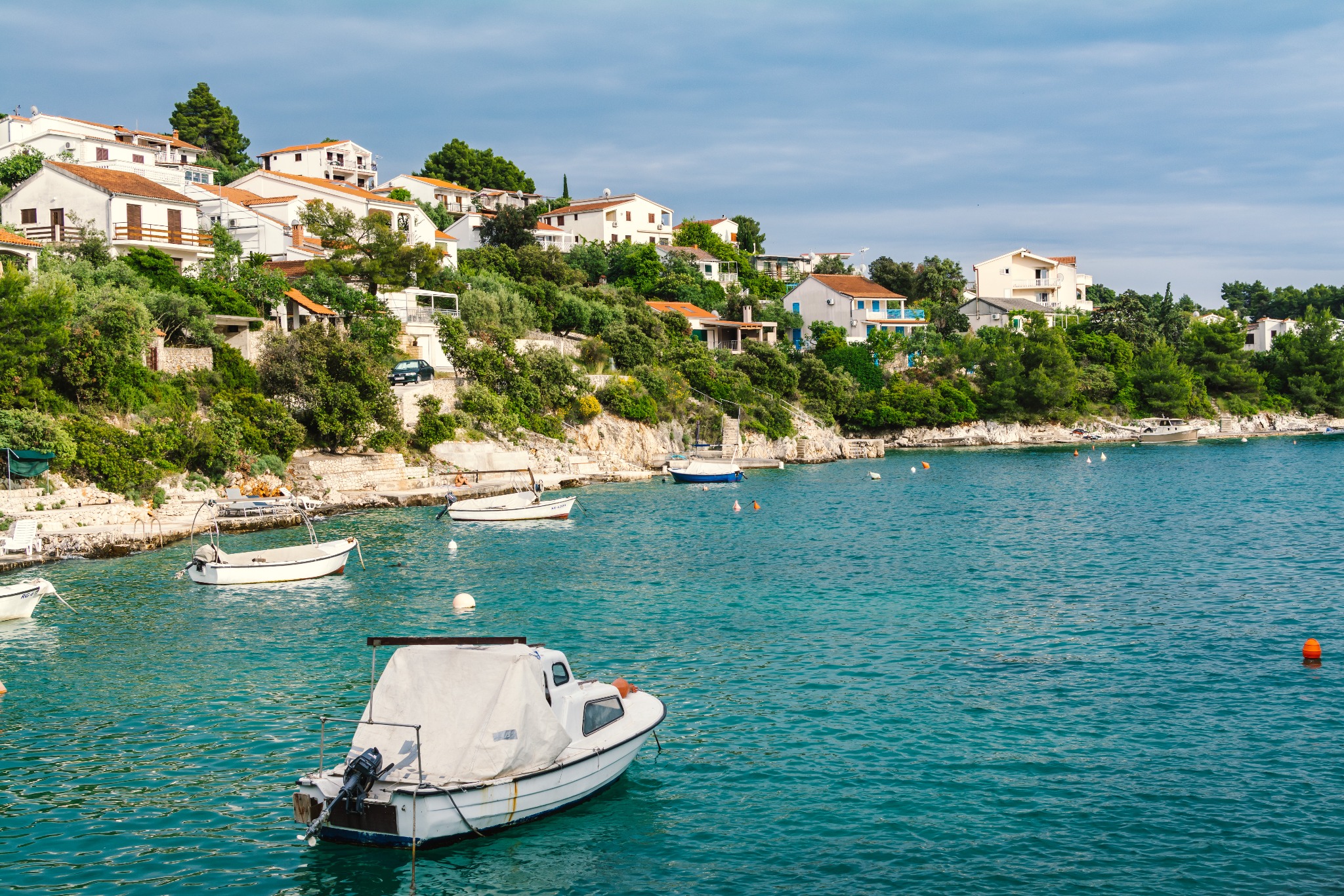 Turkusowa woda zatoki z zacumowanymi łodziami na tle białych domów na wzgórzu, Chorwacja. Widok na malownicze wybrzeże.