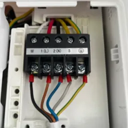 Podłączenie elektryczne klimatyzacji: widoczne kable w kolorach czarnym, brązowym, niebieskim, szarym i ż&oacute;łto-zielonym, podłączone do listwy zaciskowej w obudowie.