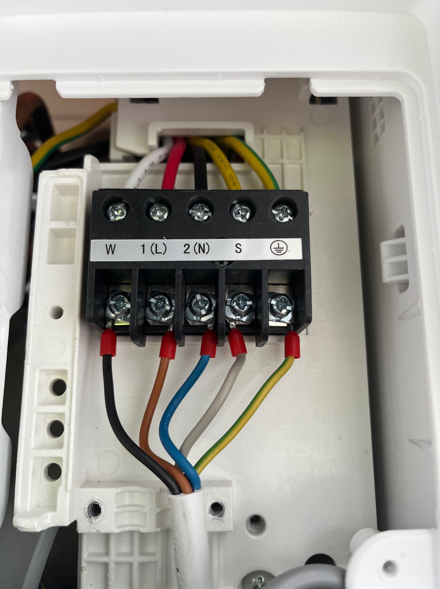 Podłączenie elektryczne klimatyzacji: widoczne kable w kolorach czarnym, brązowym, niebieskim, szarym i żółto-zielonym, podłączone do listwy zaciskowej w obudowie.