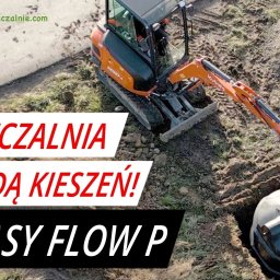 Firma Handlowo Usługowa KATKA Katarzyna Dutka - Montaż przydomowej oczyszczalni ścieków Bio Easy Flow P: minikoparka Kubota opuszcza betonowy element na zbiornik w wykopie, obok pracownik w kasku i żółtych rękawicach.