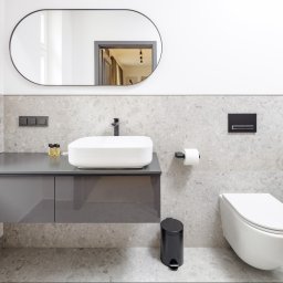 PIK ARCHITEKTURA MARIUSZ ZAŃKO - Nowoczesna łazienka z owalnym lustrem, podwieszaną szafką z umywalką, wiszącą toaletą i szarymi płytkami imitującymi kamień.
