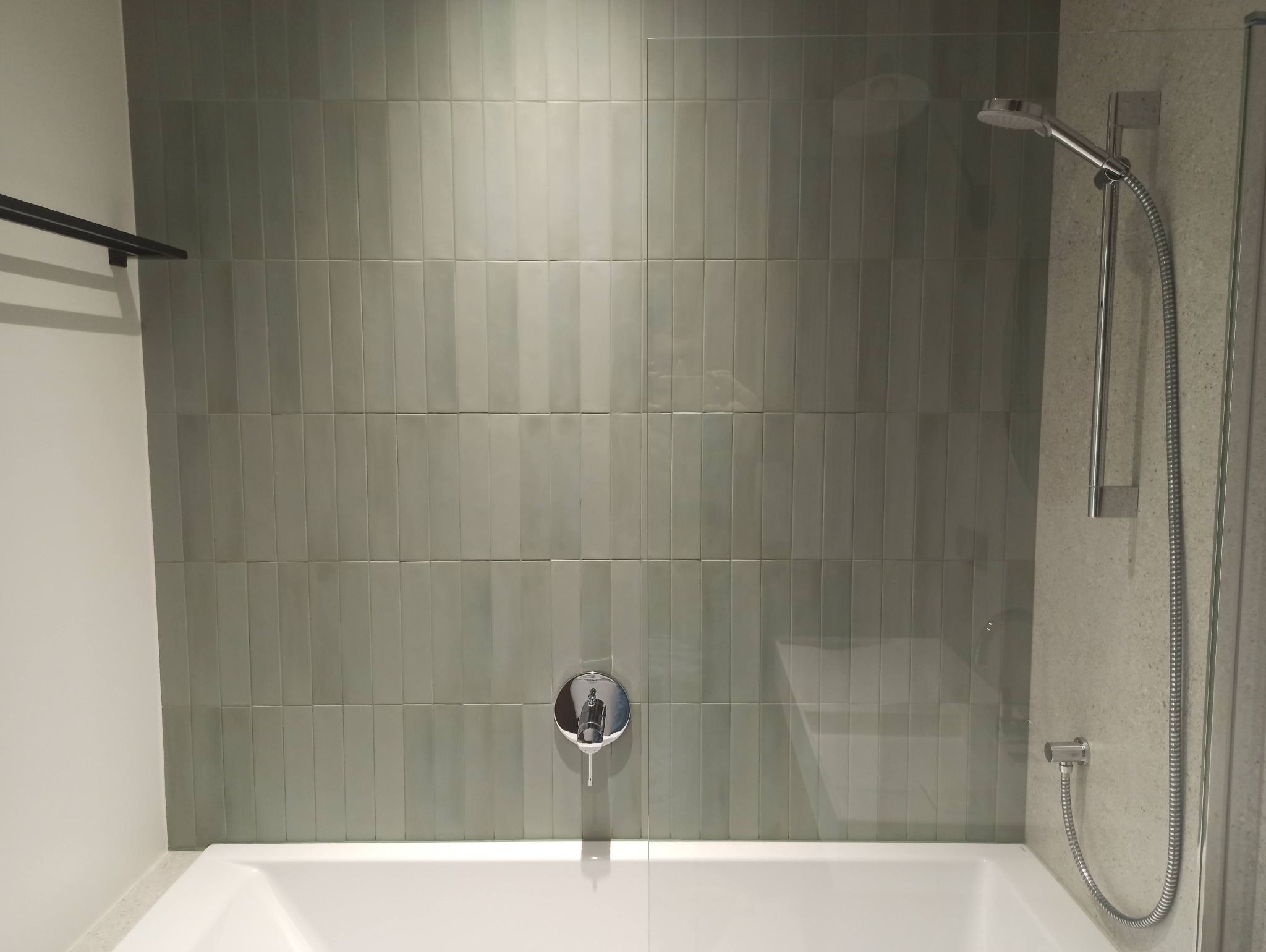 Szczegółowe ujęcie wykończonej łazienki z wanną, chromowaną baterią i prysznicem; ściany wyłożone pionowymi, szarymi płytkami o subtelnym połysku.